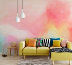 a yellow couch sitting in front of a wall with pink and orange paint on it