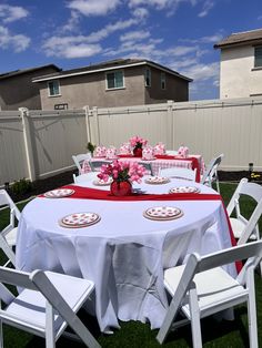 the table is set with white chairs and pink flowers in vases on red napkins