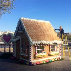 a woman standing on a ladder next to a gingerbread house shaped like a candy shop