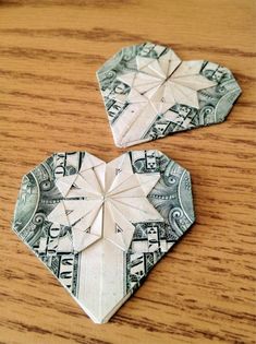 two origami hearts made out of dollar bills on a wooden table with one folded in the shape of a heart