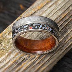 a wooden ring with silver and red inlays on the inside is sitting on a piece of wood