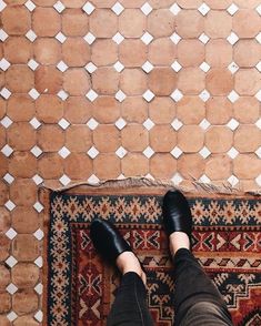 a person wearing black shoes standing in front of a rug