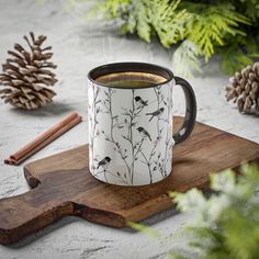 a cup of tea sitting on top of a wooden cutting board next to pine cones