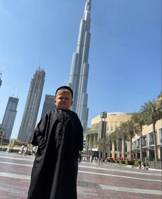 a young boy is standing in front of the burj tower, with his hands on his hips