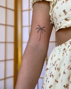 a woman's arm with a small palm tree tattoo on the left side of her arm