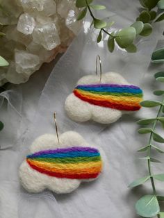 two small white clouds with rainbow colored thread on them are sitting next to some green leaves