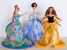 three barbie dolls are standing next to each other on a white surface, one is wearing a blue dress