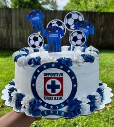 a cake with soccer decorations on it in the grass and someone holding up a cupcake