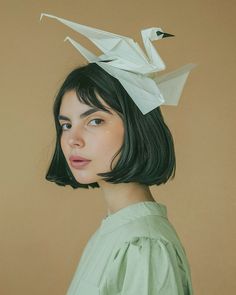 a woman with black hair wearing a white origami bird on top of her head