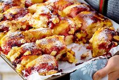 a person holding a tray full of pastries with powdered sugar on top and toppings