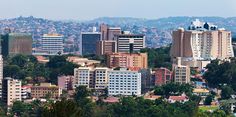 a city with tall buildings and trees in the foreground, surrounded by hills on either side