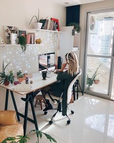 a woman sitting at a desk in front of a computer monitor with plants on it