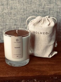 a white candle sitting on top of a wooden table next to a bag