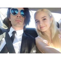 a man and woman sitting in the back seat of a car, wearing sun glasses