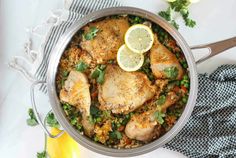 a pan filled with chicken and rice on top of a table next to lemons