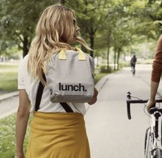 two people walking down the street with lunch bags on their backs and bicycles behind them