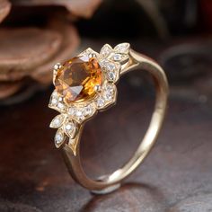 a yellow gold ring with an orange stone surrounded by white diamonds on a wooden surface