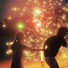 two people holding hands as fireworks go off in the background