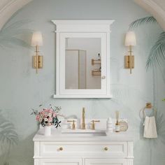 a white bathroom with palm leaves on the wall and mirror above it, along with two gold faucets