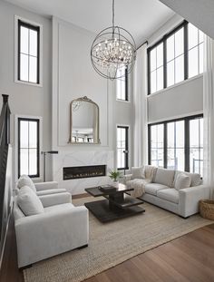 a living room filled with furniture and a fire place under a chandelier in front of two large windows