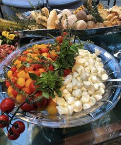 an assortment of vegetables on a platter in front of other foods and desserts