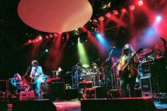 a group of people that are on stage with some lights in the background and one person playing guitar