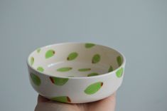 a hand holding a green and white bowl with leaves on the inside, in front of a gray background