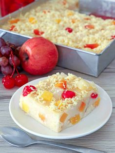 a piece of cake on a white plate next to a pan of fruit and a fork