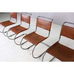 four brown leather chairs with chrome frames and wheels on the legs, all lined up in a row