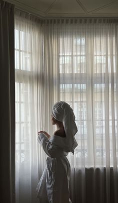 a woman standing in front of a window with a towel on her head and looking out the window