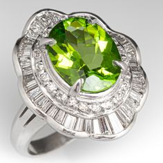 The ring is centered with one (1) oval mixed cut natural peridot set into a four-prong setting. The center stone is bordered with twenty two (22) channel/prong set, round brilliant cut diamonds and forty (40) channel set, tapered baguette cut diamonds. The ring measures 22.6mm at the top, rises 9.8mm above the finger, tapering to 2.7mm wide and 1.0mm thick at the base of the shank. The ring is currently sized to a 6.75. Oval Tsavorite Ring With Gemstone Accents, Luxury Oval Peridot Rings, Elegant Lime Green Ring With Center Stone, Elegant Lime Green Gemstone Rings, Elegant Peridot Ring With Center Stone, Formal Lime Green Rings With Center Stone, Elegant Lime Green Rings For Anniversary, Elegant Lime Green Rings For Formal Occasions, Elegant Lime Green Jewelry With Center Stone