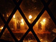 some candles are lit in a window with diamond shaped glass panels on the outside and inside