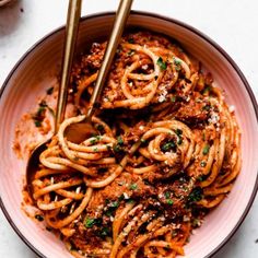 a bowl filled with spaghetti and sauce on top of a table next to a fork