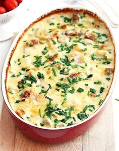 a casserole dish with meat and vegetables in it on a wooden table next to tomatoes