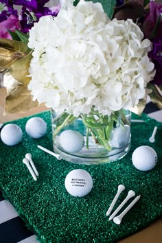 a vase filled with white flowers next to golf balls and tees on a green mat