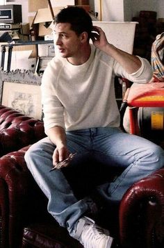 a young man sitting on top of a red leather couch in a living room next to a chair