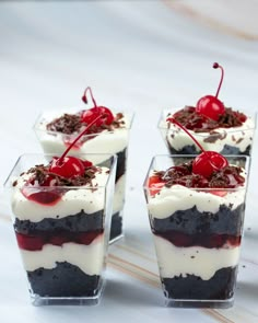 four desserts with cherries and whipped cream in small glass dishes on a table