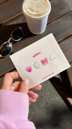 a person holding up a piece of paper with hearts on it next to a cup of coffee