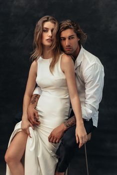 a man and woman are posing for a photo in front of a dark background, with one holding the other's leg