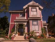 the house is painted pink and has flowers on the front porch, along with steps leading up to it