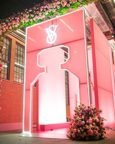 a large pink sign sitting in the middle of a building with flowers growing out of it