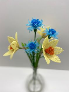 three yellow and blue flowers in a glass vase on a white table top with grey background