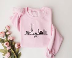 "Introducing our stylish and comfortable Unisex sweatshirt featuring the iconic Paris skyline embroidered on the front. Made from high-quality pre-shrunk 50% cotton and 50% polyester, this sweatshirt is designed to keep you warm and cozy on chilly days, while also adding a touch of French flair to your wardrobe. The Paris skyline embroidery is a standout feature of this sweatshirt, showcasing the city's most famous landmarks including the Eiffel Tower, the Arc de Triomphe, and the Notre-Dame Cathedral. You have the option of choosing between black or white stitches, depending on your personal preference. Either way, the pattern is expertly stitched onto the soft and breathable fabric, ensuring that it will stand the test of time and maintain its vibrant colors wash after wash. The maximum Skyline Embroidery, Paris Sweatshirt, Paris Gifts, Paris Shirt, Style Français, Famous Landmarks, The Eiffel Tower, Embroidered Sweatshirts, Unisex Design