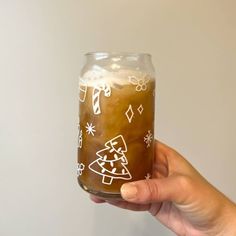 a hand holding a glass with liquid in it and christmas decorations painted on the inside