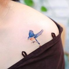 a small blue bird tattoo on the back of a woman's shoulder and chest