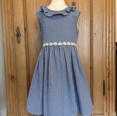 "Beautiful sleeveless gingham dress made from navy and white medium weight 100% cotton. Classic design with ruffle embellishment at collar that extends to v shaped back neckline, lined bodice, back zipper and self fabric ties with back bow. Adorned with white and yellow daisy trim around the waist. Perfect summer party or special occasion dress. Size 5 from the pattern. Please measure a well fitting dress for proper fit due to the variability of sizing in patterns of different vintage and style. width at chest is 14\"/35 cm waist to hem length 16\"/40cm Can purchase with a little growing room and cinch with waist ties. All my dresses are one of a kind. Bespoke dresses in this style can be obtained in sizes 2-5." Gingham Dress With Smocked Back For Garden Party, Navy Sleeveless Dress With Ruffles, Summer Gingham Dresses With Smocked Back, Navy Ruffle Dress For Summer, Fitted Gingham Sundress, Cotton Gingham Dress With Lace Trim, Gingham Cotton Dress With Lace Trim, Spring Gingham Dresses Lined, Sleeveless Gingham Dress With Ruffles