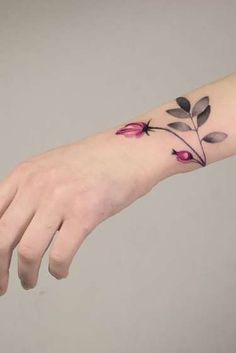 a woman's hand with a flower tattoo on the left wrist and pink flowers on the right arm