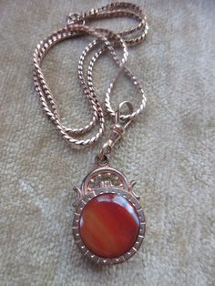 Antique agate watch fob necklace in gold fill. Our antique watch fob is adorned with a stone on each side. A carnelian colored banded agate on one side a a dark stone on the reverse make the double sided fob a striking piece. It suspends from a 16'' gold fill chain that closes with an old fashioned C thumb spring clasp. A swivel hook acts as the bail and brings the pendant to a length of one and seven eighths of an inch x .75''. The fob is older than the chain which may date to the 1930s. These pieces exhibit age appropriate wear with some scratching and finish loss. This estate found necklace will make an interesting layering necklace with your other antique pieces. Gold Carnelian Jewelry With Polished Finish, Gold Agate Jewelry With Polished Finish, Vintage Polished Pendant Jewelry, Vintage Pendant Jewelry With Polished Finish, Formal Carnelian Cameo Jewelry, Antique Gemstone Jewelry For Memorial, Formal Cameo Jewelry In Carnelian, Formal Cameo Carnelian Jewelry, Formal Agate Pendant Jewelry