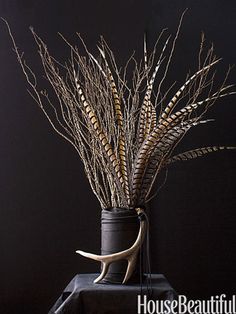 a vase filled with dried plants on top of a black table next to a wall