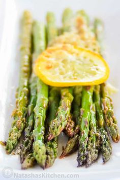 asparagus with lemon wedges and parmesan cheese on the side in a white serving dish